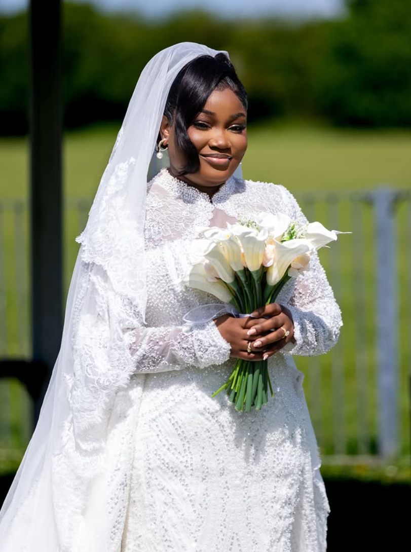 Bride in a pearl-embellished gown and veil holding her bouquet in natural daylight