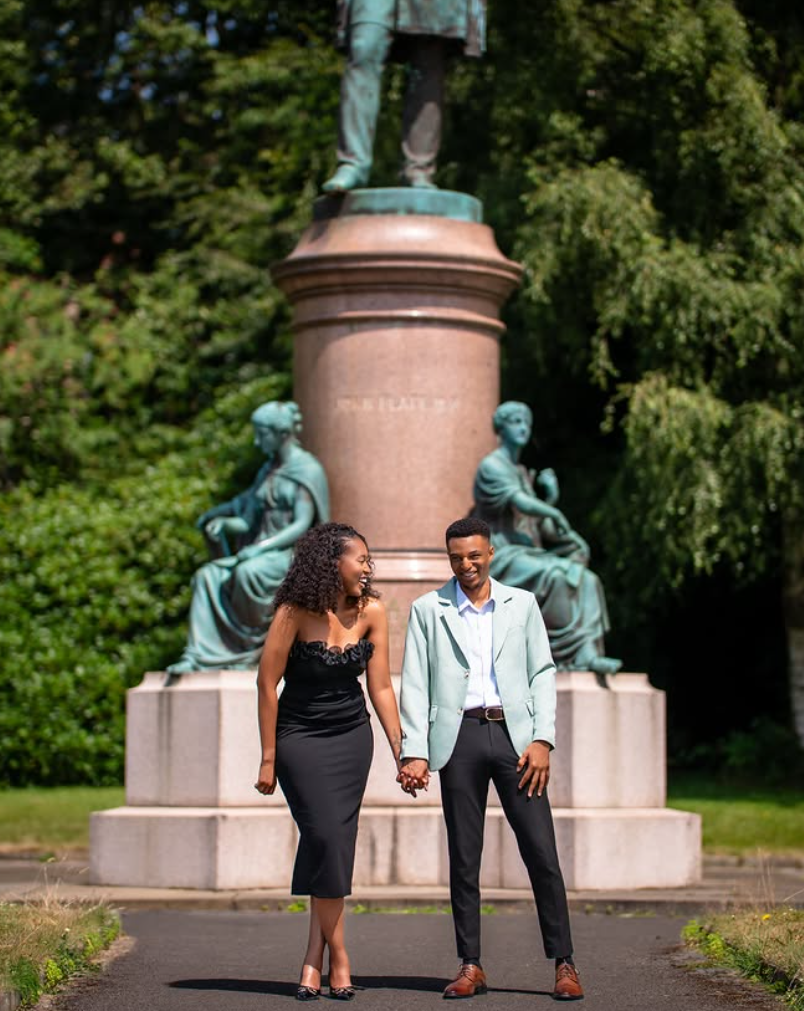 Couple holding hands and laughing in front of a park monument during a couples shoot
