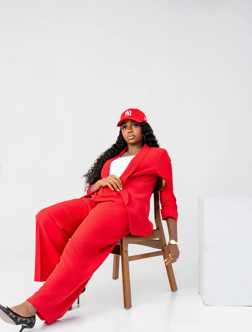 Studio portrait of a woman in a red suit seated on a wooden chair against a white backdrop